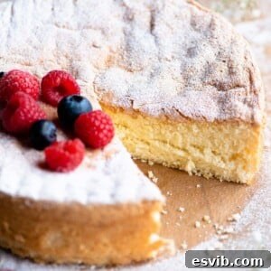 A square image of an Italian sponge cake (Pan di Spagna) close up with a slice cut out and berries on top.