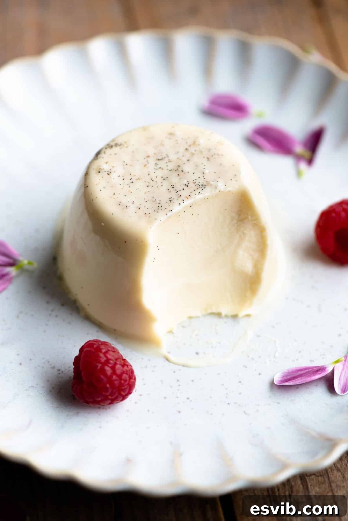 A vanilla panna cotta on a plate with a bite out and raspberries at the side.