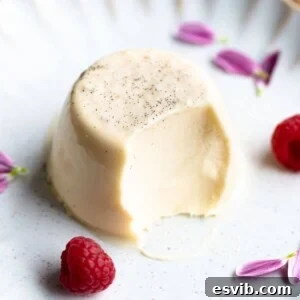 A close up of a vanilla panna cotta on a white plate with raspberries at the side.