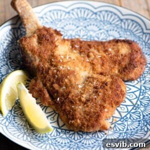 A cropped square image of a golden Veal Milanese on a blue plate with a lemon wedge.