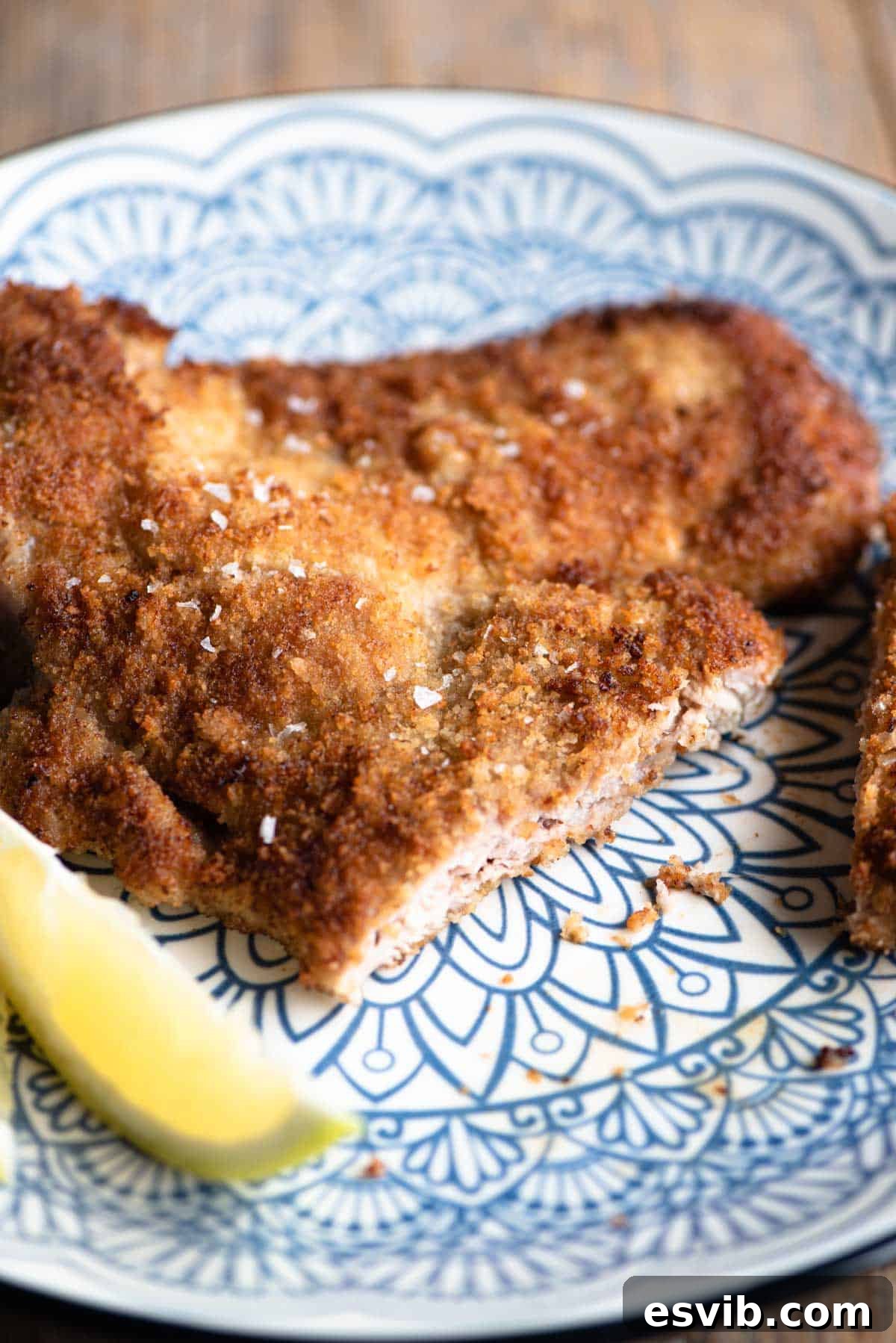 A close-up shot of a sliced Veal Milanese on a plate, revealing its tender interior and crispy golden crust.