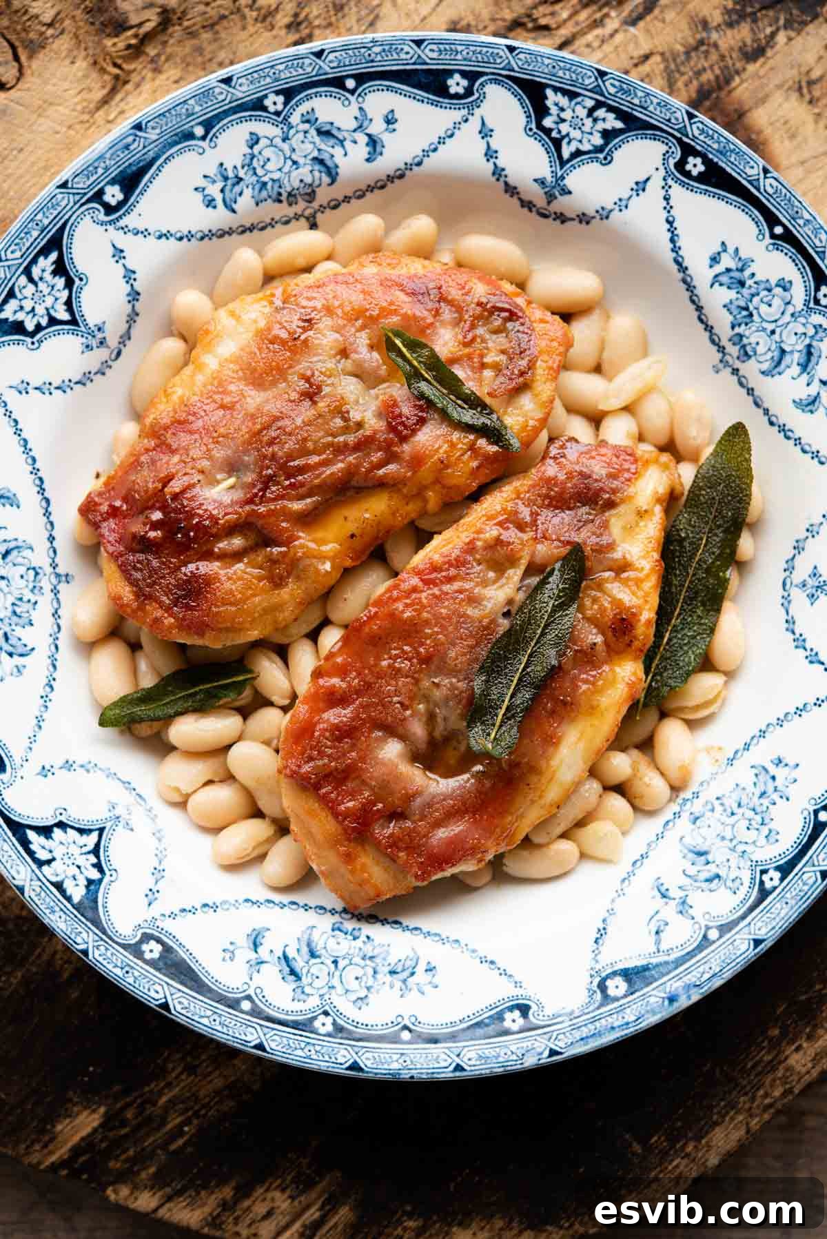 Two pieces of chicken saltimbocca on a plate on top of cannellini beans.