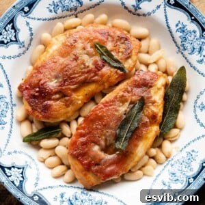 A cropped square image of chicken saltimbocca in a blue bowl on top of cannellini beans.