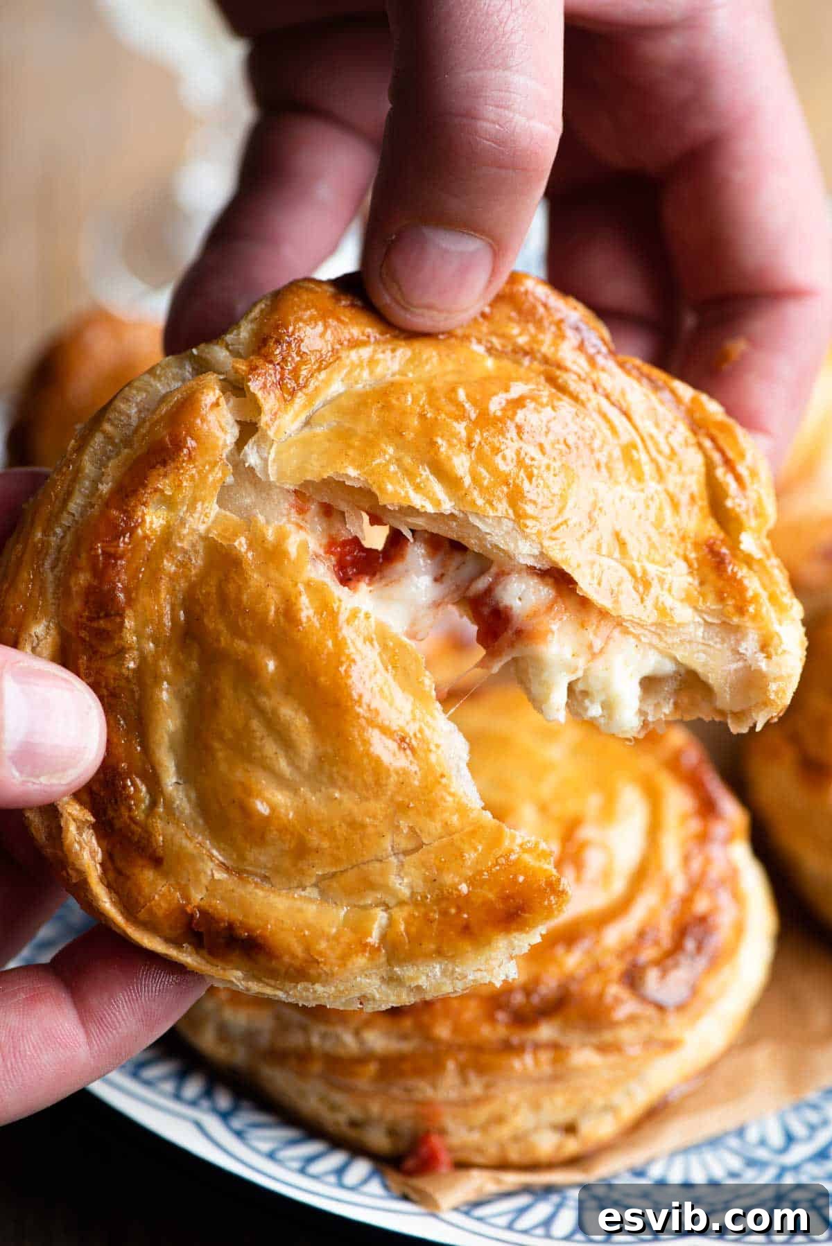 Rustic Lecce Tomato and Mozzarella Pastries 7 Two hands gently tearing open a freshly baked Rustico Leccese, revealing its warm, cheesy tomato filling oozing out, highlighting the delicious textures inside.