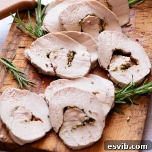 A close up cropped image of roast pork loin sliced on a wooden board.