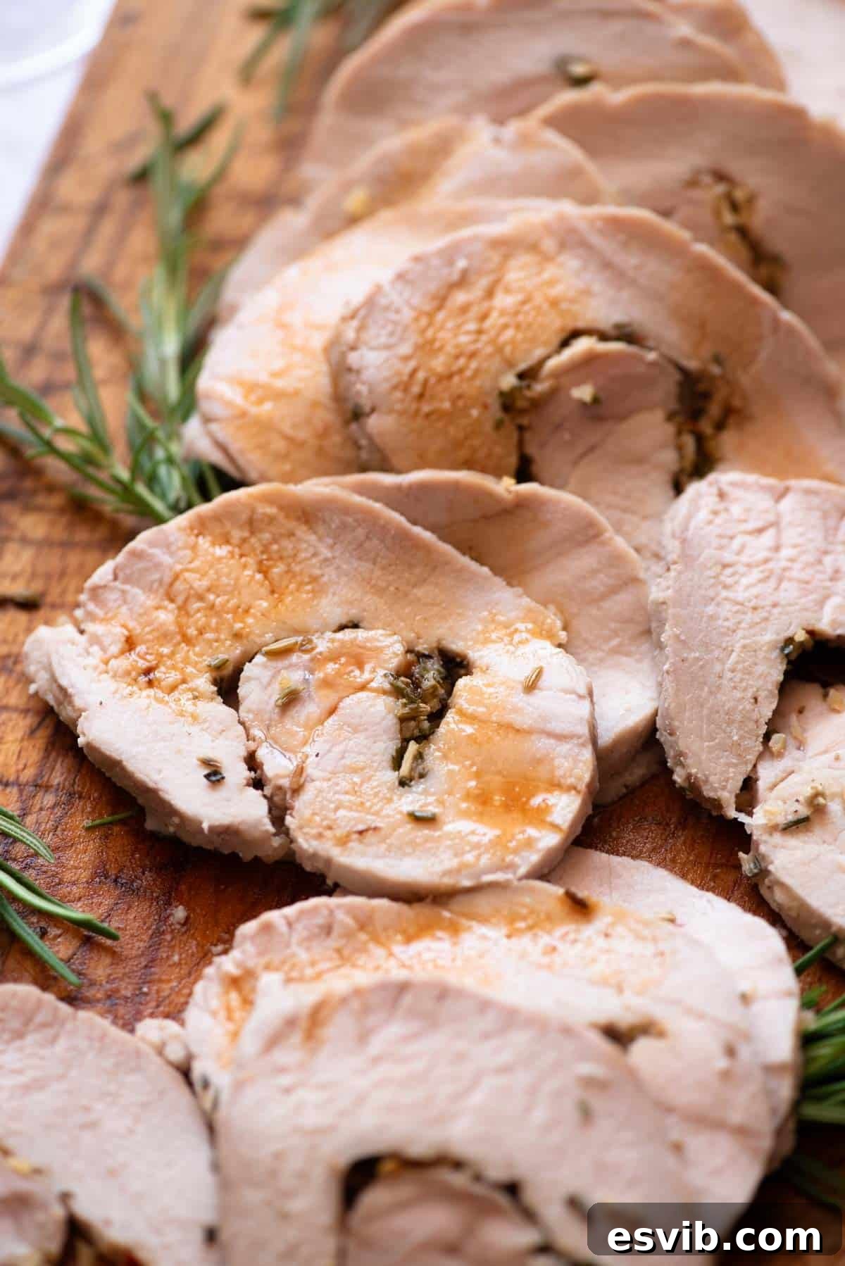 A close up of Italian stuffed pork loin on a wooden board drizzled with gravy.