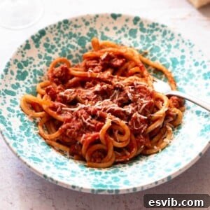 A cropped square image of Tuscan sausage pasta in a blue speckled bowl.