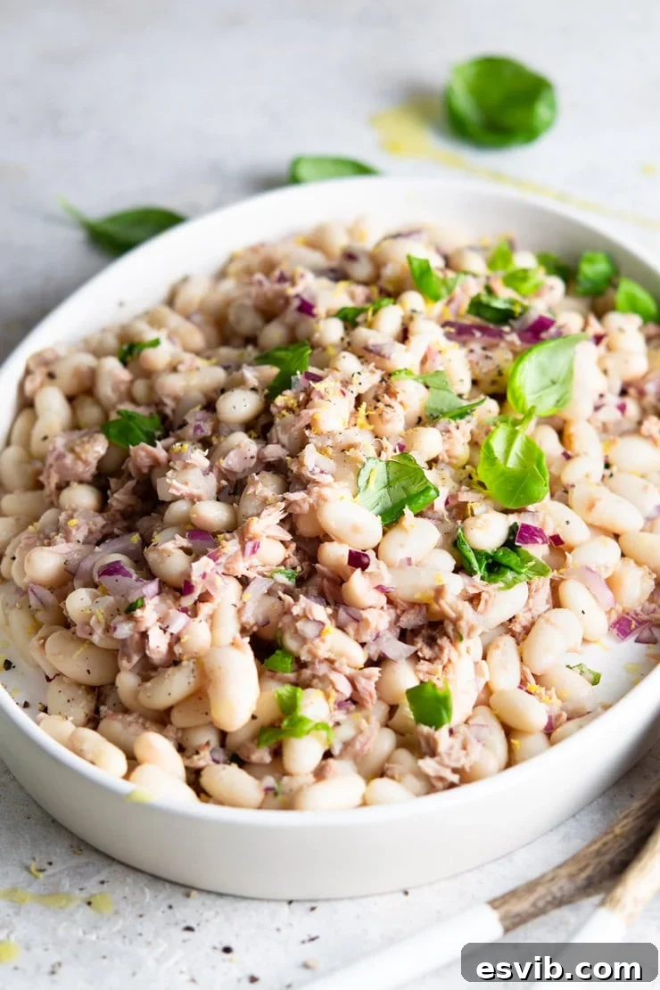 A side shot of a white bean salad with tuna and basil on a white serving plate, highlighting its fresh appeal.