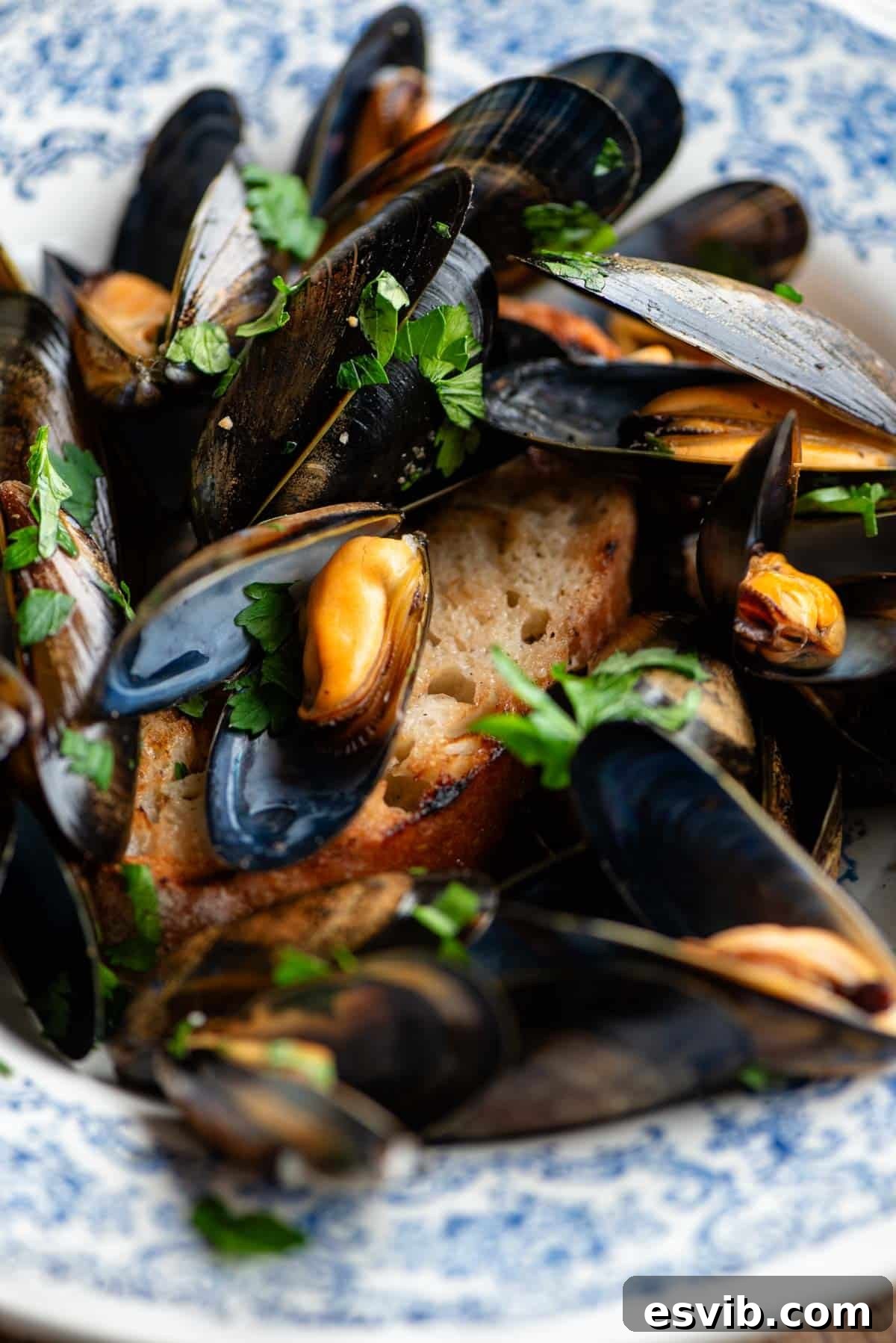A close-up shot of perfectly cooked peppered mussels served atop a slice of crispy char-grilled ciabatta bread, showcasing the rich broth and fresh parsley garnish.