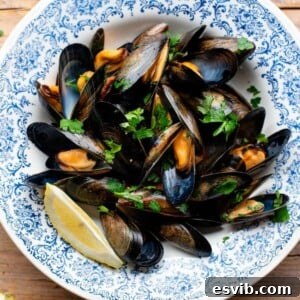 A cropped image of succulent peppered mussels (Impepata di Cozze) artfully arranged in a blue bowl, garnished with vibrant fresh parsley and a wedge of bright lemon.