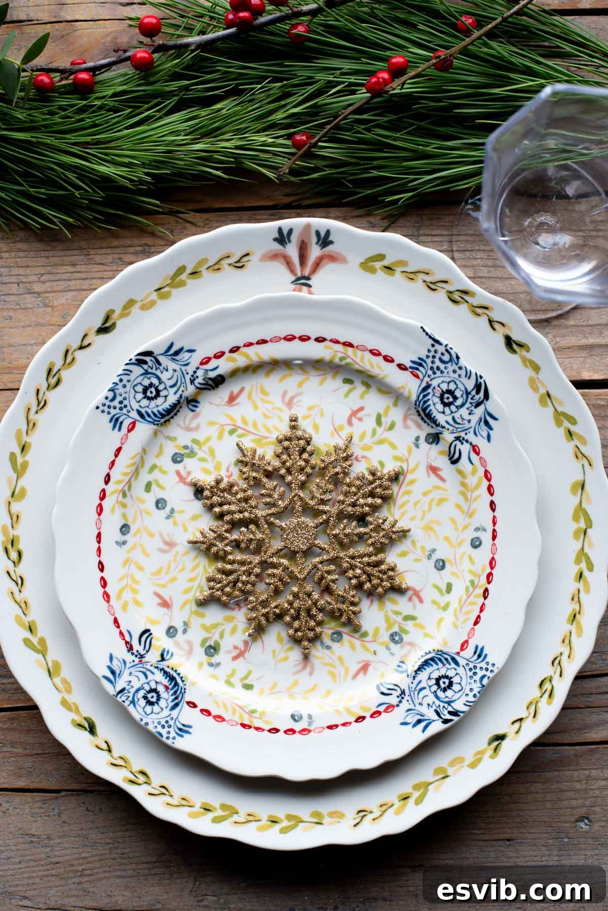 A beautifully set Christmas table with festive plates, a wooden tabletop, and elegant foliage decorations.