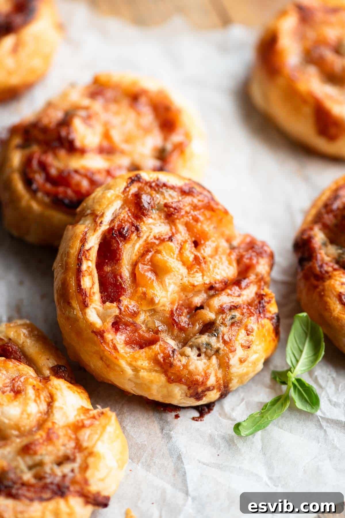 A close-up shot of several freshly baked, golden-brown pizza pinwheels, showcasing their flaky layers and delicious melted fillings, resting on a wooden board.