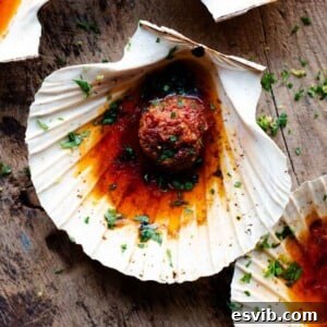 A close up of a scallop in a shell topped with nduja garlic butter.