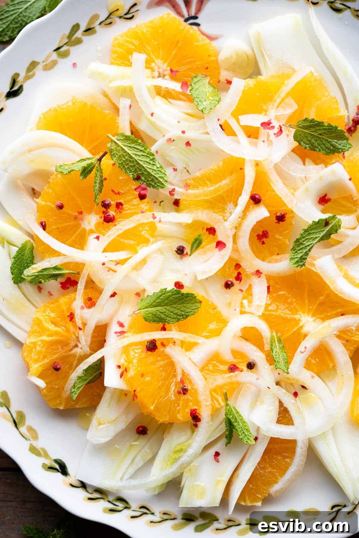Sicilian Sunshine Salad 6 A close-up view of a beautifully composed fennel and orange salad, highlighted with thinly sliced white onion, fresh mint leaves, and scattered pink peppercorns.