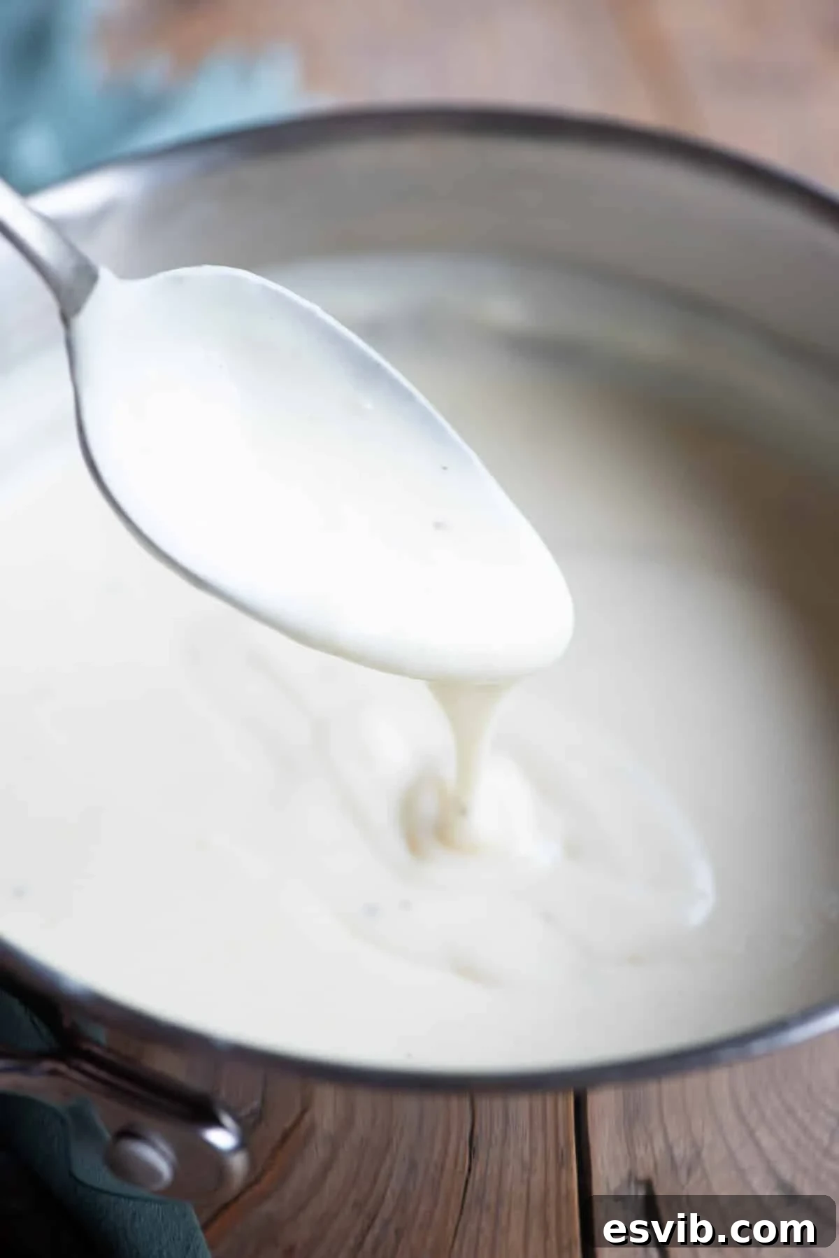 Classic Italian Béchamel Sauce 7 A close up of Italian Besciamella sauce in a pot with some dripping off a spoon, showing its creamy texture.