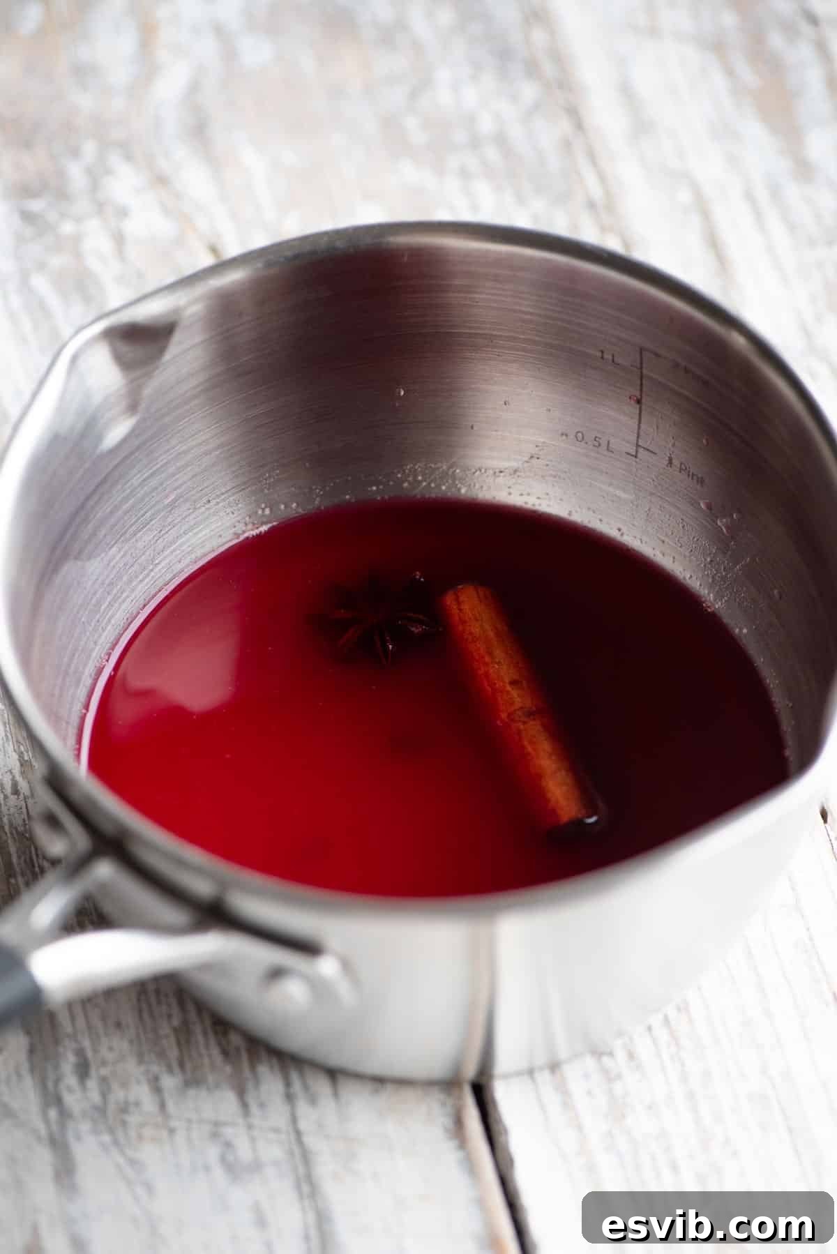 A small pot with cranberry juice and Christmas spices inside sitting on a white wooden table, illustrating the infusion process.