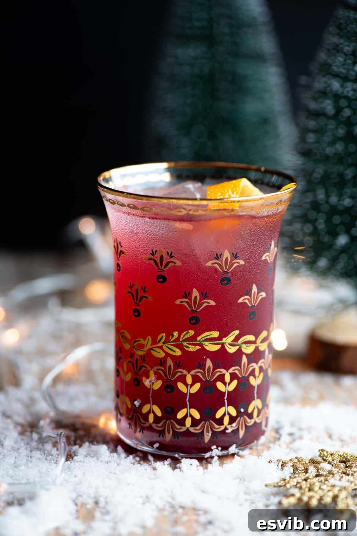 A close up side shot of a Cranberry and Prosecco cocktail sitting on a wooden table with snow all around, emphasizing its holiday ambiance.