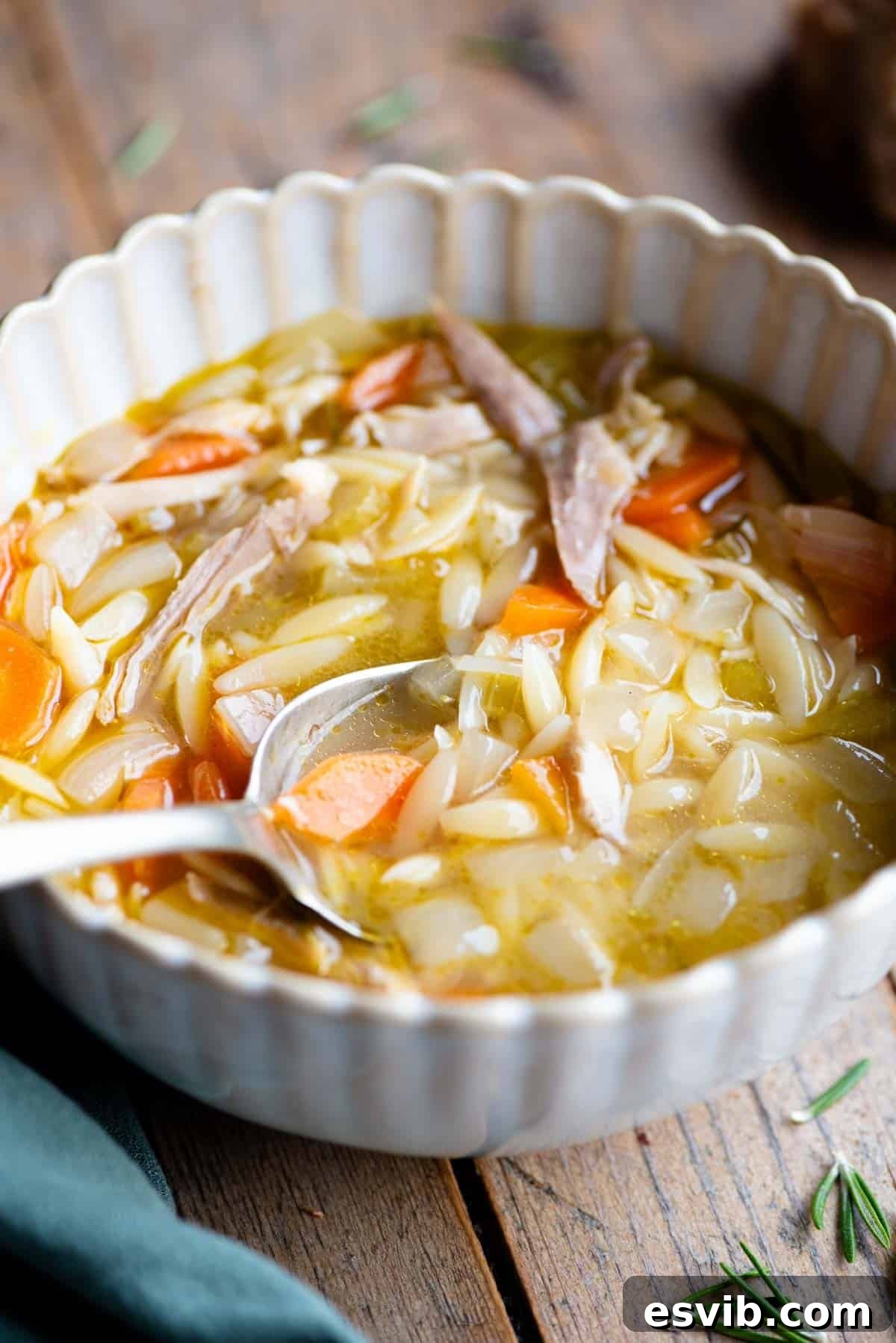 A close-up side view of a steaming bowl of Lemon Chicken Orzo Soup, showcasing the delicate pasta, tender chicken, and colorful vegetables, with a spoon resting in the bowl, ready to be enjoyed.