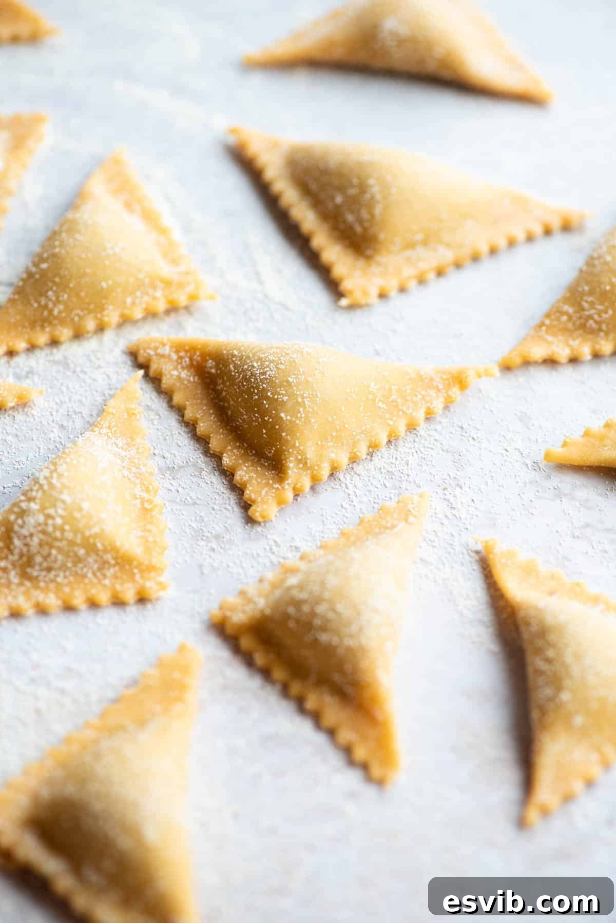 A close-up side view of meticulously crafted fresh Triangoli pasta, neatly arranged on a light grey board, showcasing their perfect triangular form and readiness for cooking.