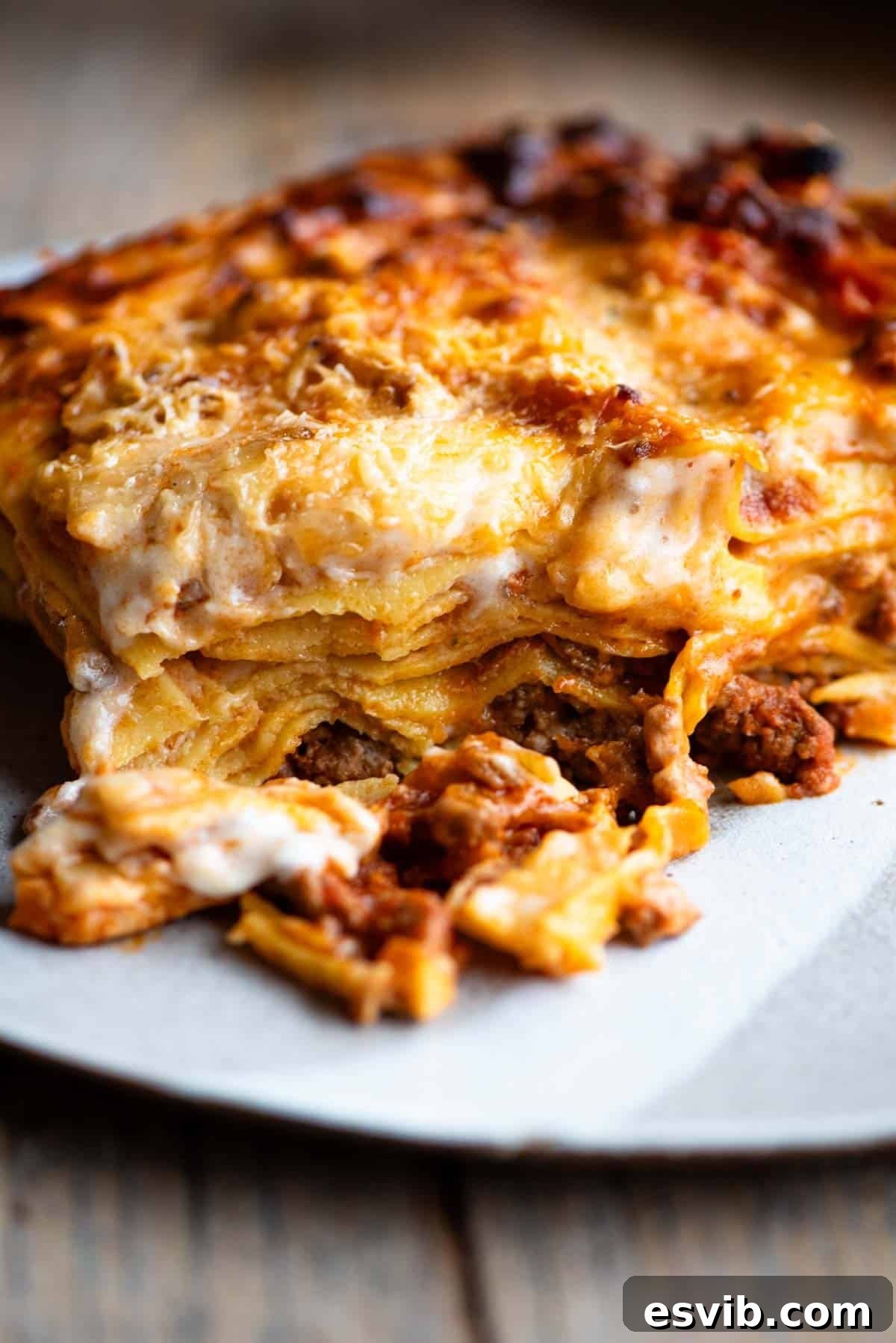 Lamb Ragù Lasagna with Pecorino Bechamel 2 A perfectly portioned slice of lamb lasagna, showcasing its layers of ragu, pasta, and bechamel, presented on a plate on a rustic wooden surface, ready to be enjoyed.