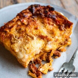A close-up of a perfectly cooked slice of lamb lasagna on a plate, with a fork resting beside it, highlighting its delicious layers.