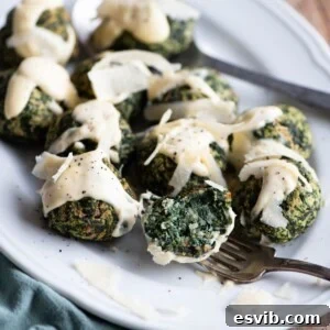 A close-up of beautifully baked spinach balls on a white serving plate, artistically drizzled with a rich Parmigiano cream, inviting a bite.
