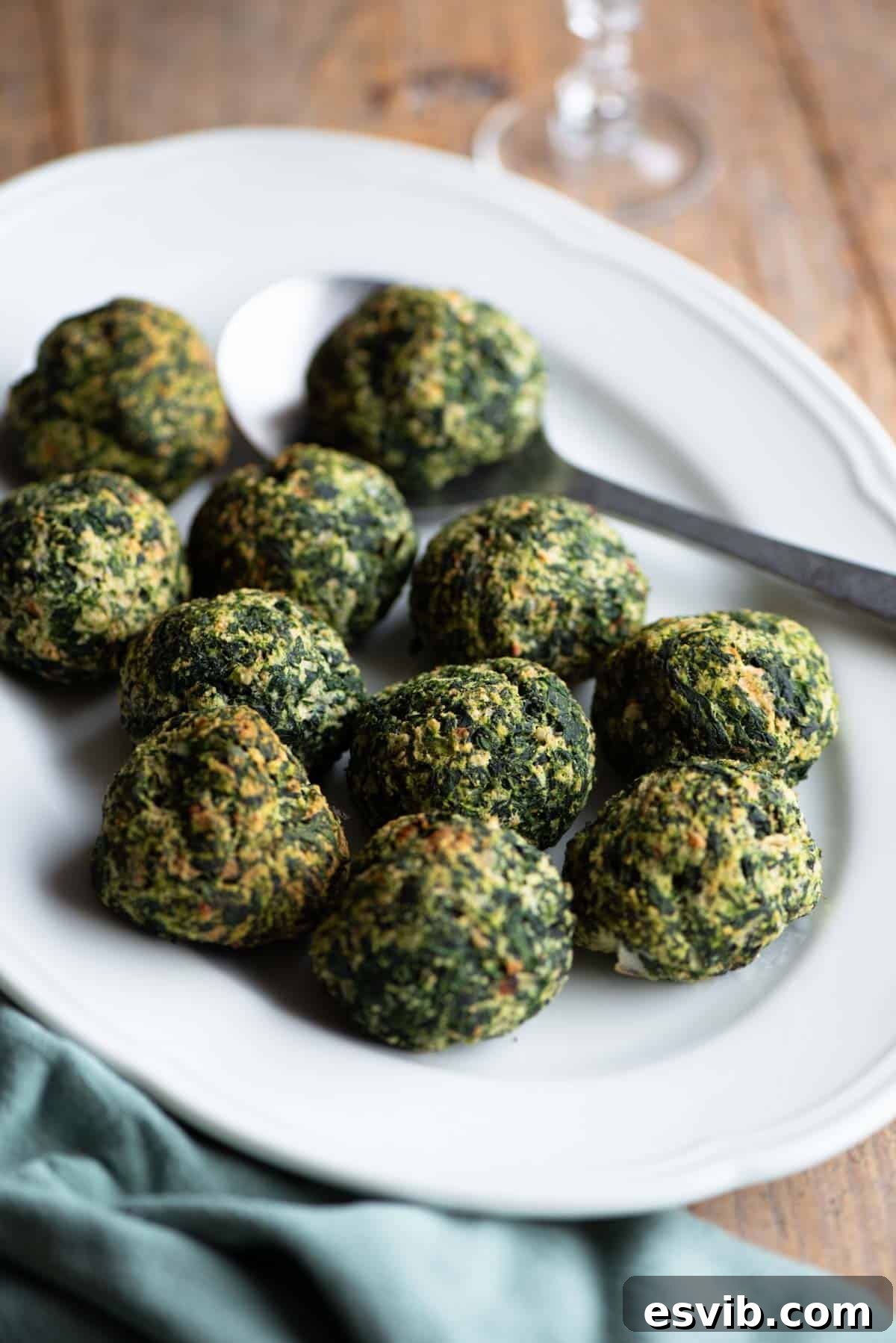 A stunning close-up of baked spinach balls resting on a pristine white serving plate, accompanied by an elegant serving spoon, ready to be enjoyed.