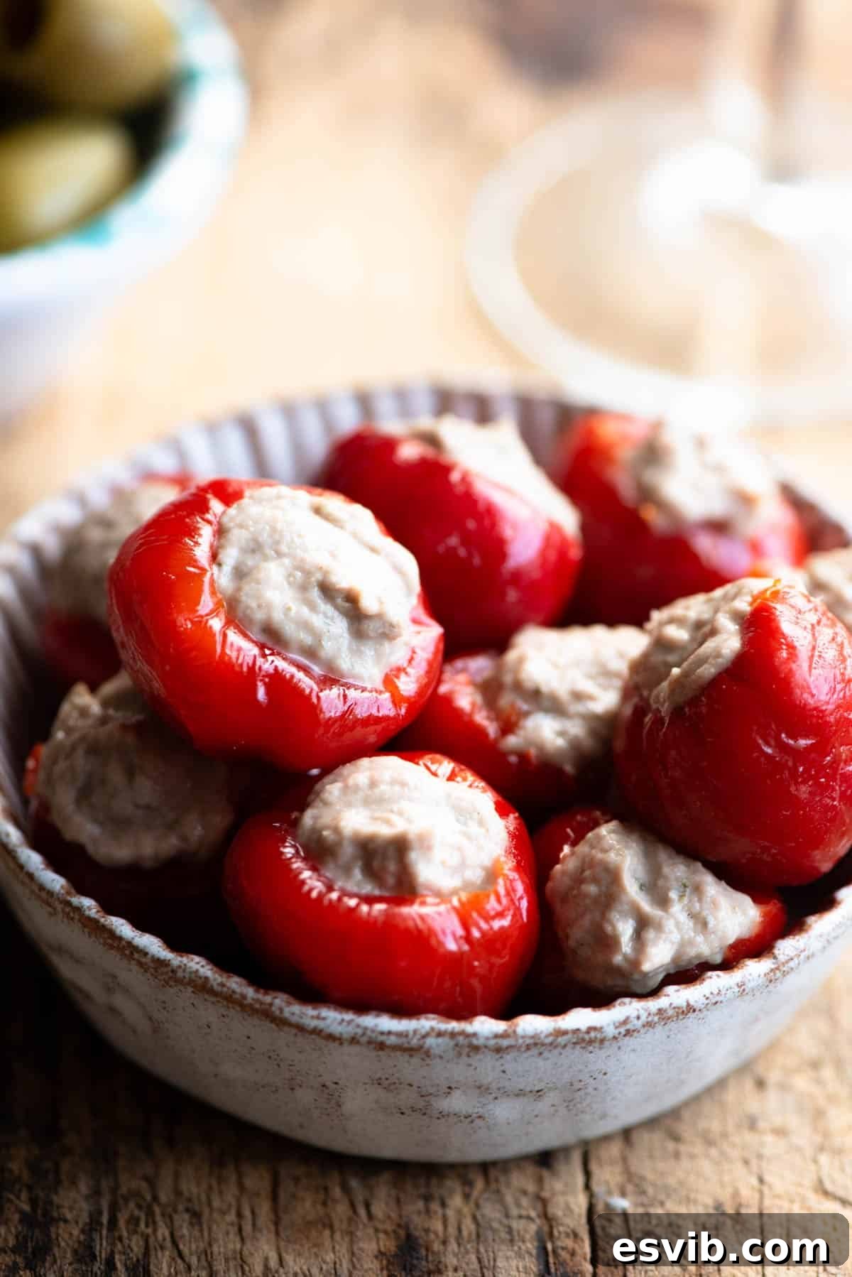 A close-up shot of beautifully arranged tuna stuffed cherry peppers in a small serving dish on a rustic wooden surface.