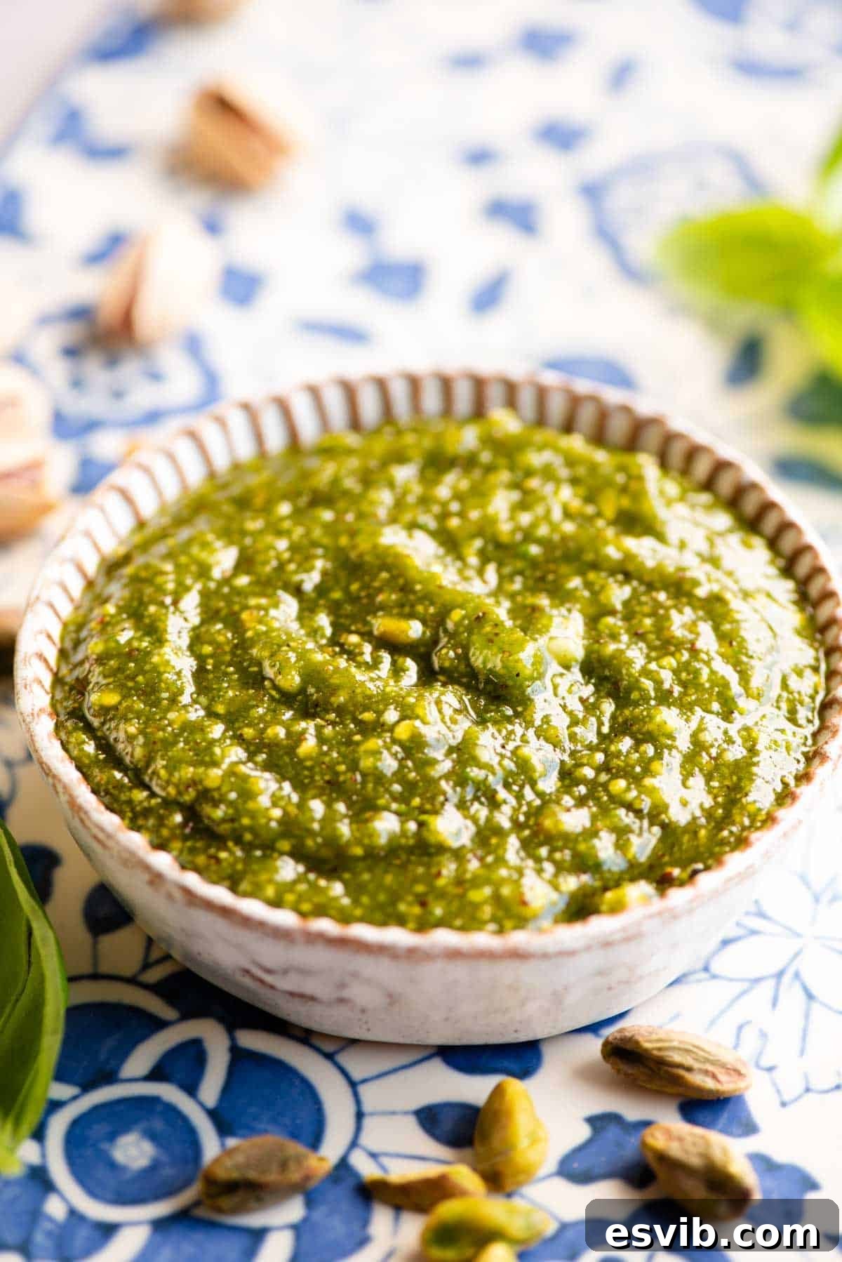 Pistachio pesto in a small round dish sitting on a blue patterned board. A rich green sauce ready to be enjoyed.