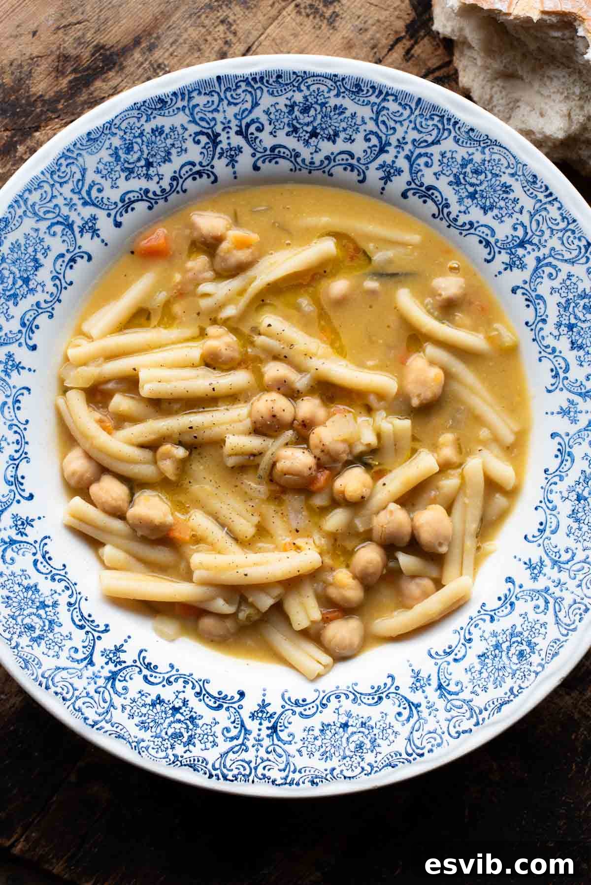 An overhead shot of a vibrant bowl of Pasta e Ceci, an Italian chickpea and pasta soup, served on a rustic wooden surface. The soup features short pasta, tender chickpeas, and a sprinkle of fresh rosemary.