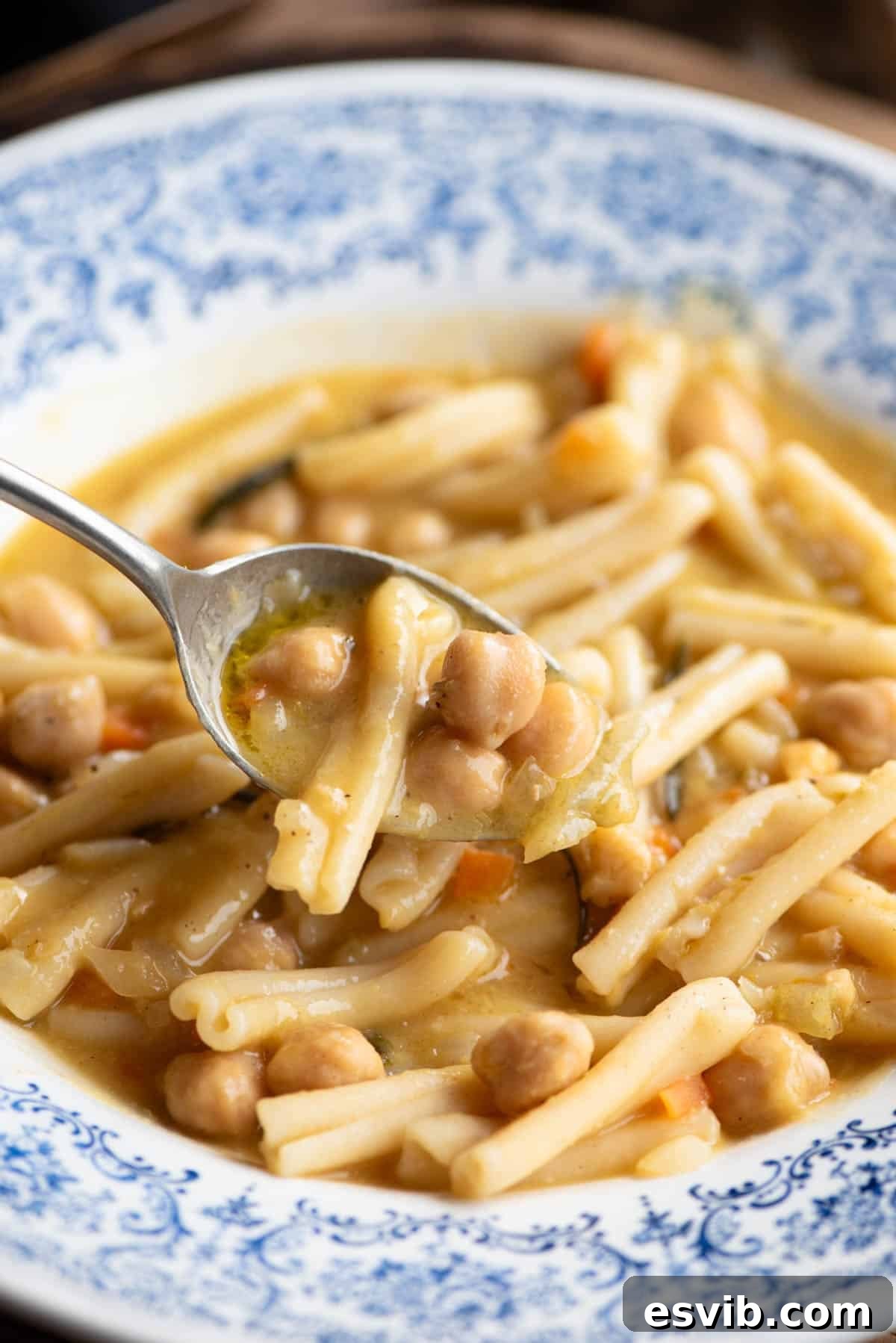 A close-up shot of a spoonful of Pasta e Ceci, showcasing the tender pasta and chickpeas in a rich, creamy broth, held over a beautiful blue ceramic bowl.