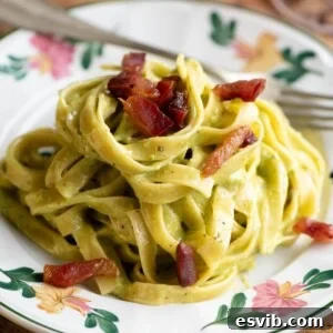 A cropped square image of pistachio pasta on a floral patterned plate topped with crispy guanciale (bacon).