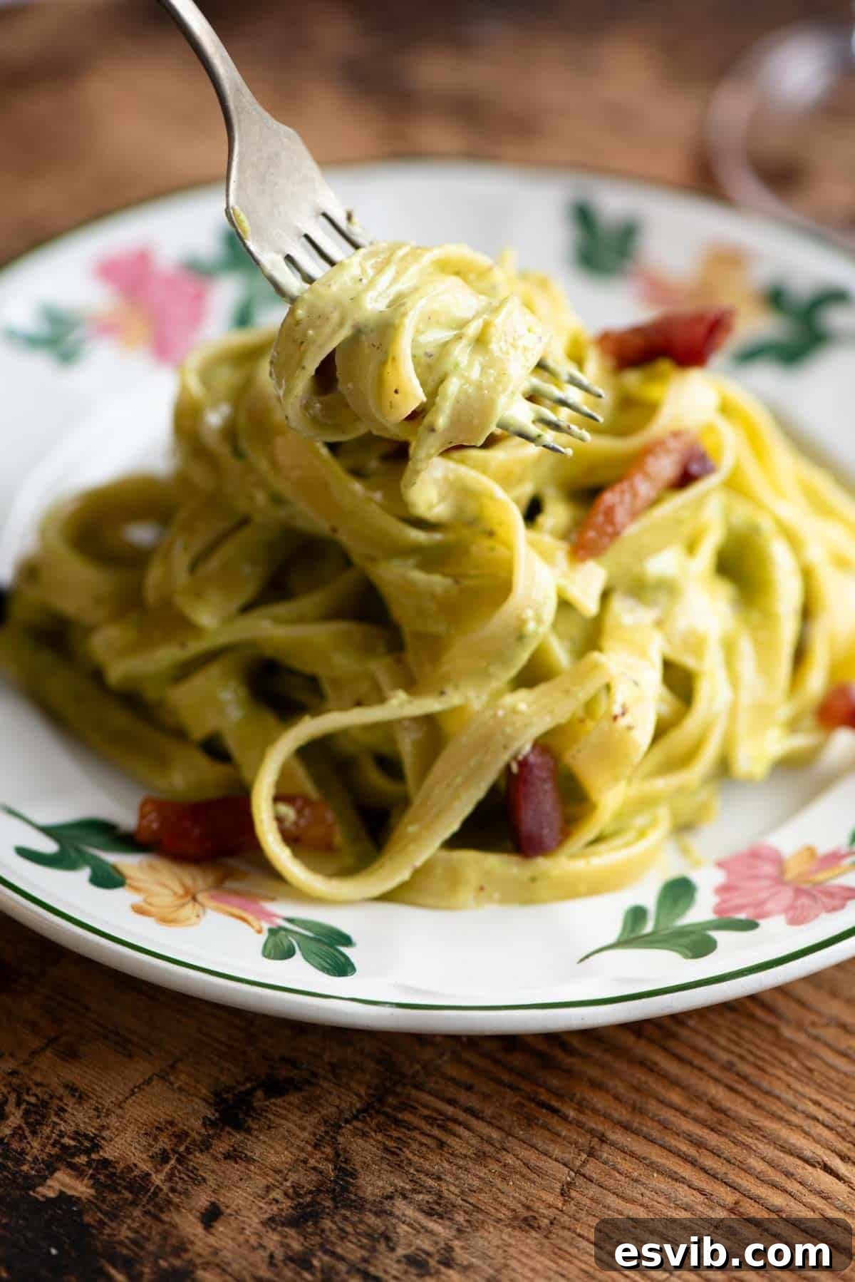 A fork picking up some tagliatelle with pistachio cream sauce from a floral patterned plate.