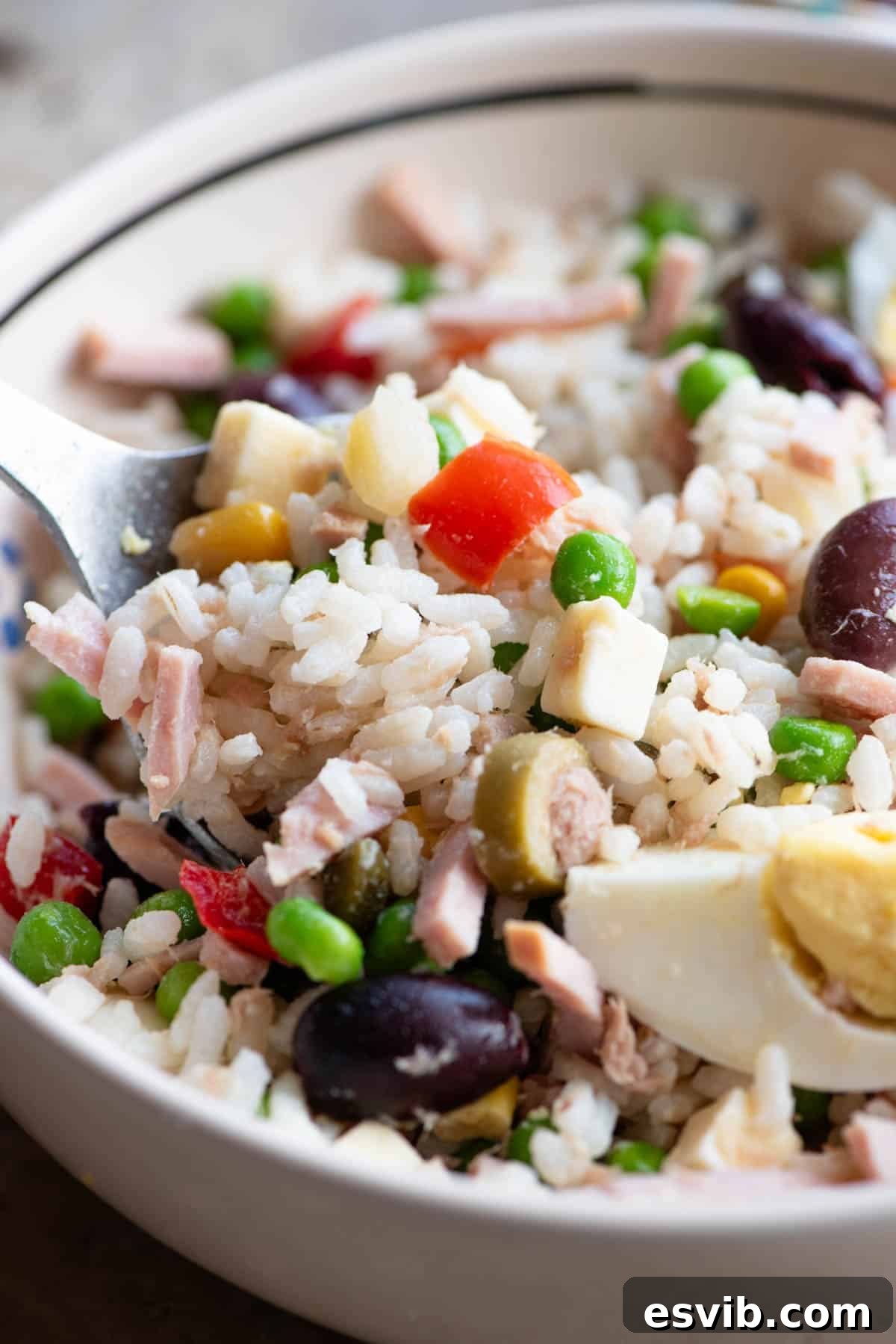 A close up of an Italian rice salad in a bowl with mixed vegetables, ham, tuna and hard-boiled eggs, highlighting the vibrant colors and textures.