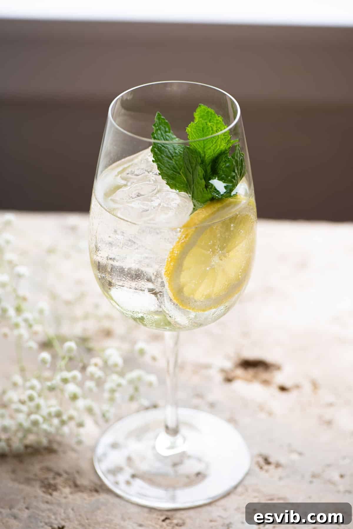 Sparkling Elderflower Delight 4 A hugo spritz cocktail on a stone worktop garnished with lemon and mint leaves, bathed in natural light.