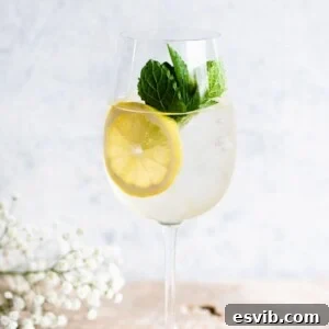 A close up cropped image of a Hugo Spritz on a light work surface garnished with lemon and mint.