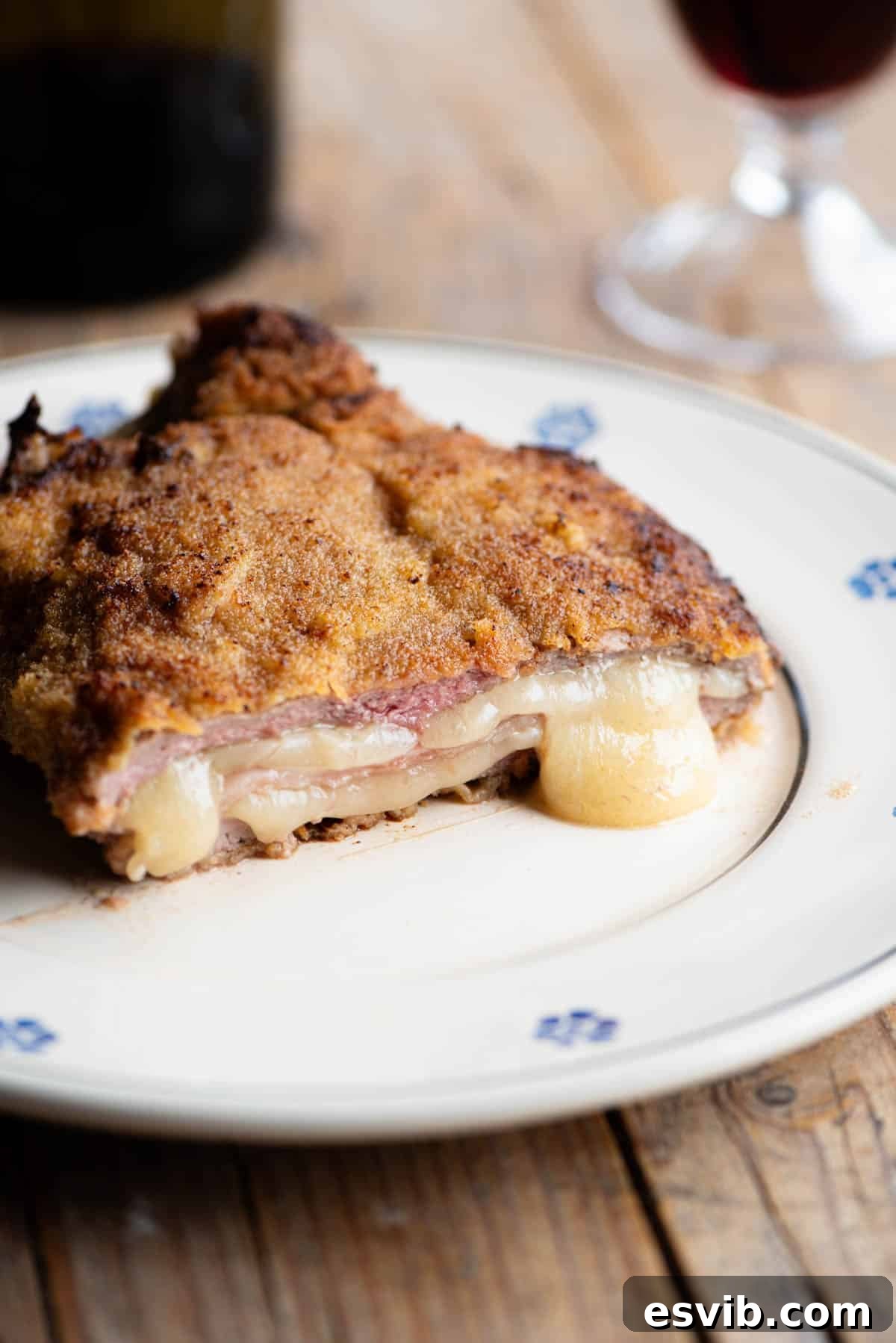 An exquisite close-up of an Italian breaded veal chop (Costoletta alla Valdostana) expertly sliced in half, revealing its luscious interior of melted Fontina cheese and tender ham, which gently oozes out onto the plate.
