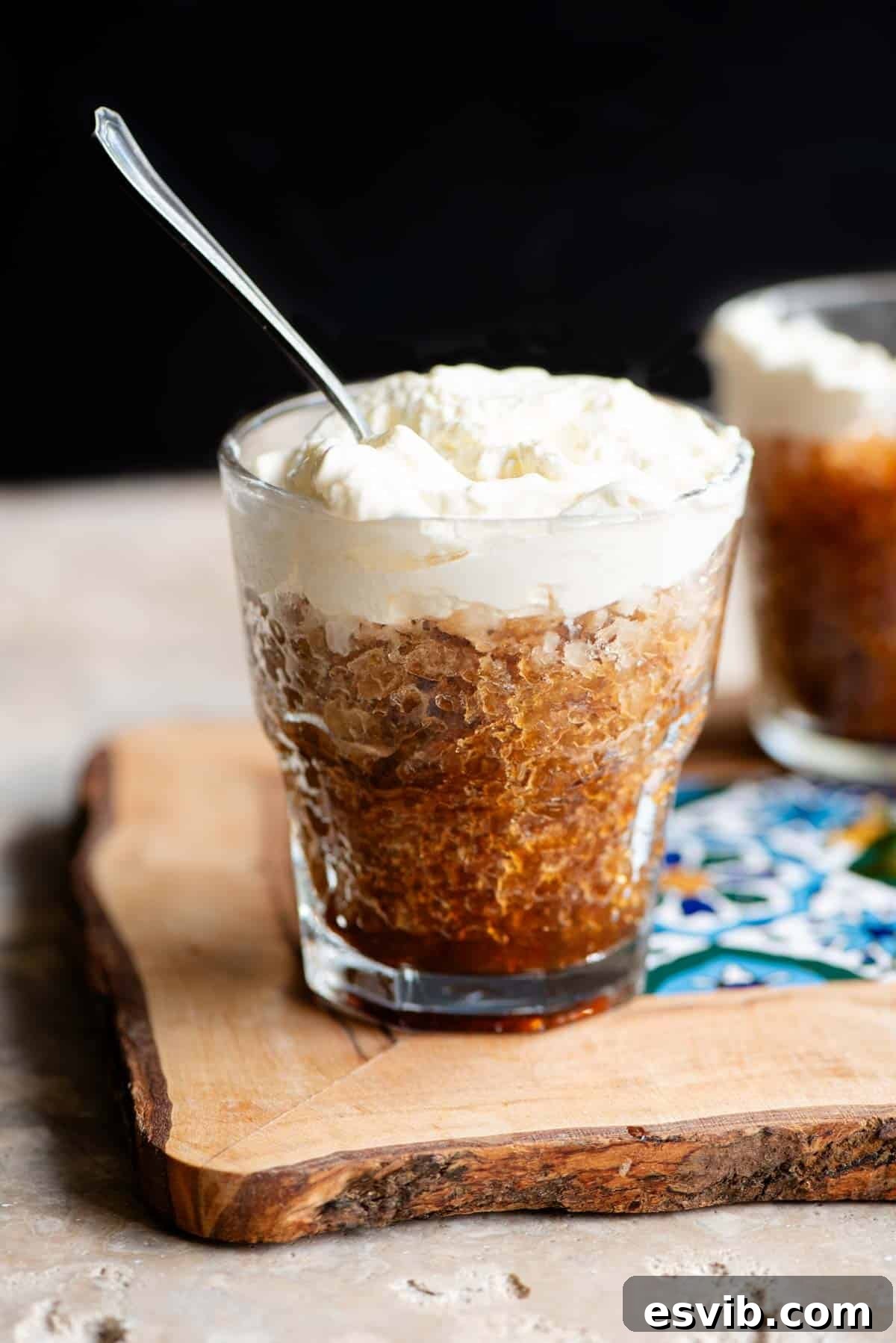 A small glass of coffee granita topped with whipped cream and a spoon in it, showcasing its refreshing texture.