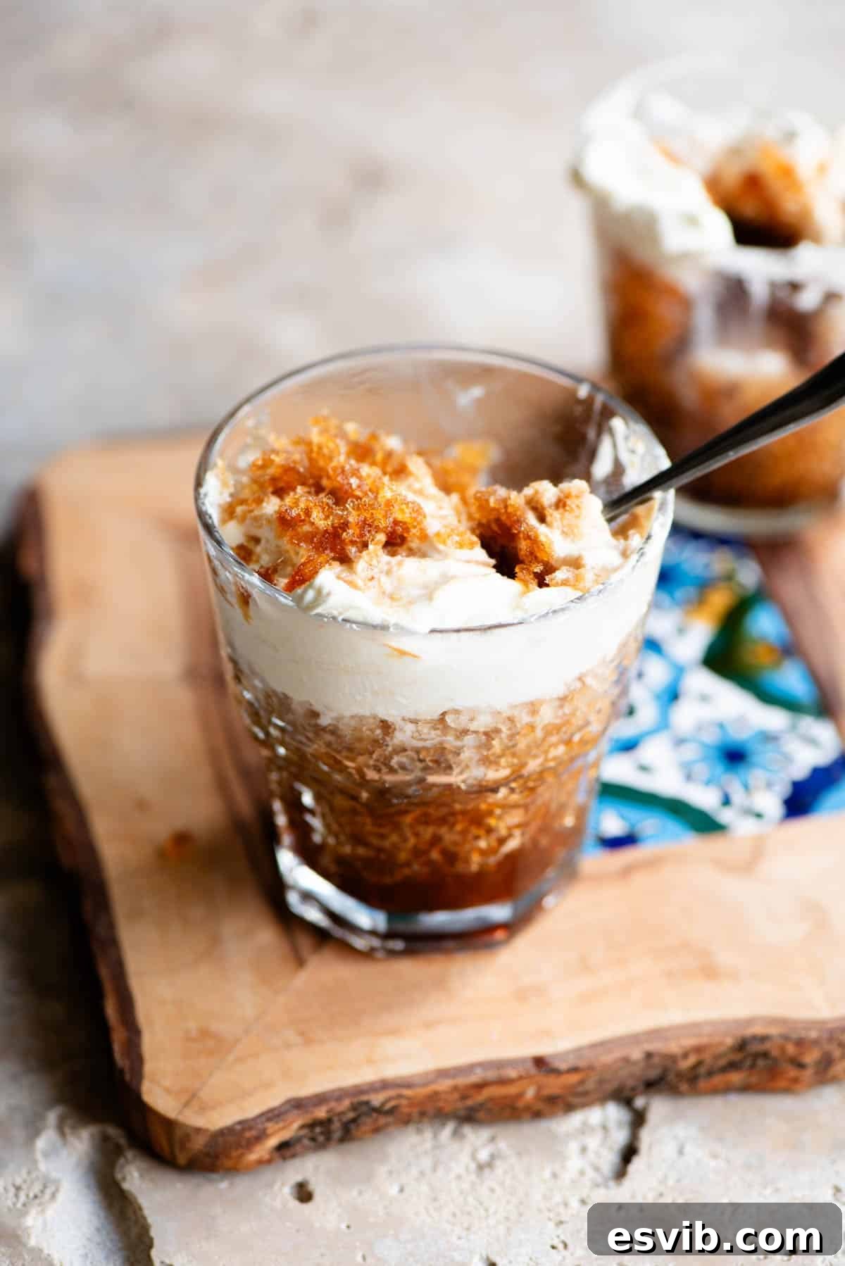 A glass filled with beautifully textured coffee granita and topped with whipped cream, sitting on a wooden serving board with a patterned tile.