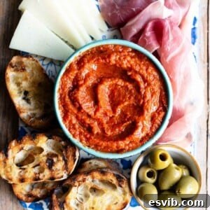A cropped image of Ajvar, a red pepper dip in a blue bowl surrounded by antipasti. A rustic and appealing shot.