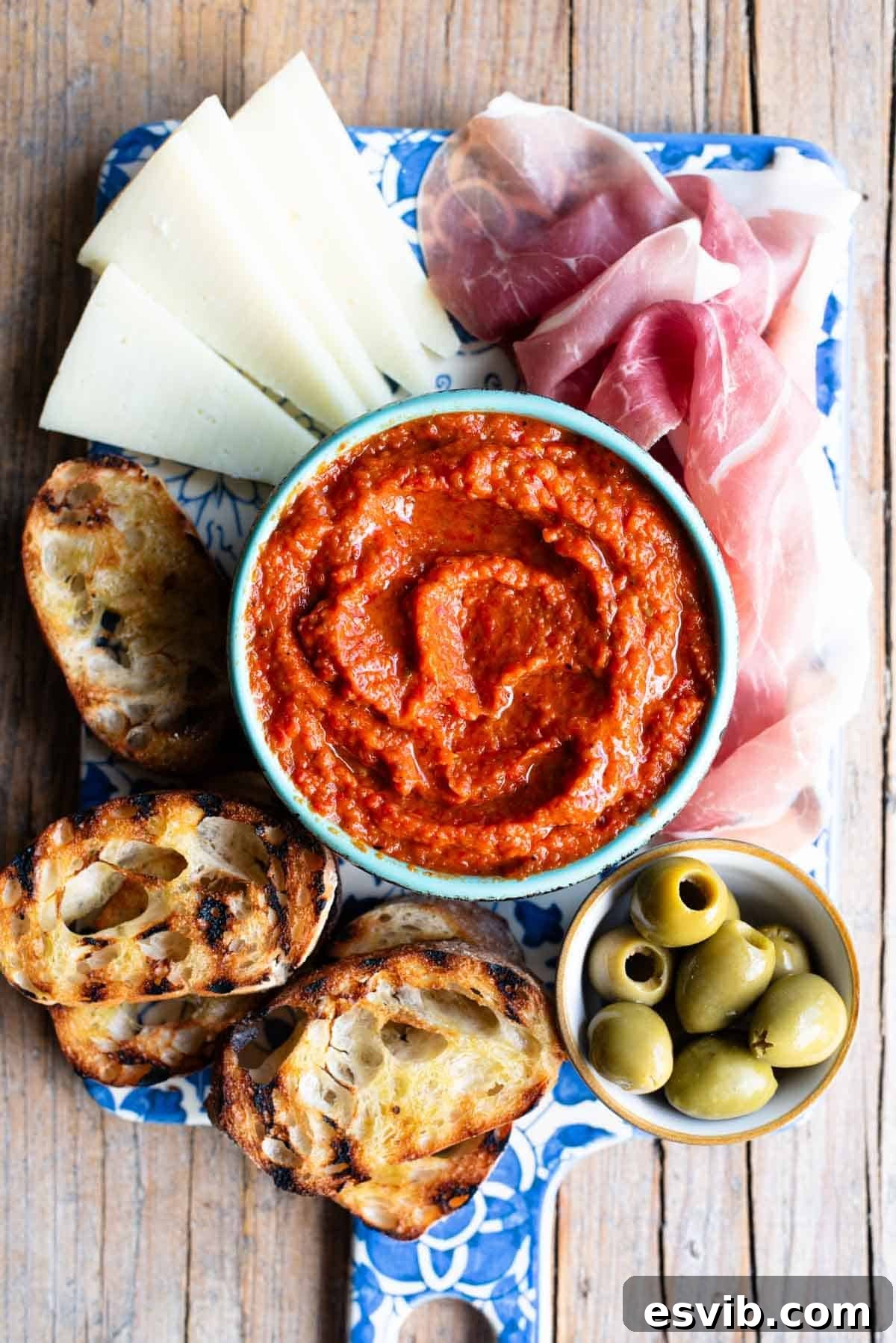 Ajvar: Smoky Roasted Red Pepper Spread 7 An overhead shot of Ajvar spread in a blue bowl sitting on a serving board with cured meats, cheese and olives, showcasing its versatility for entertaining.