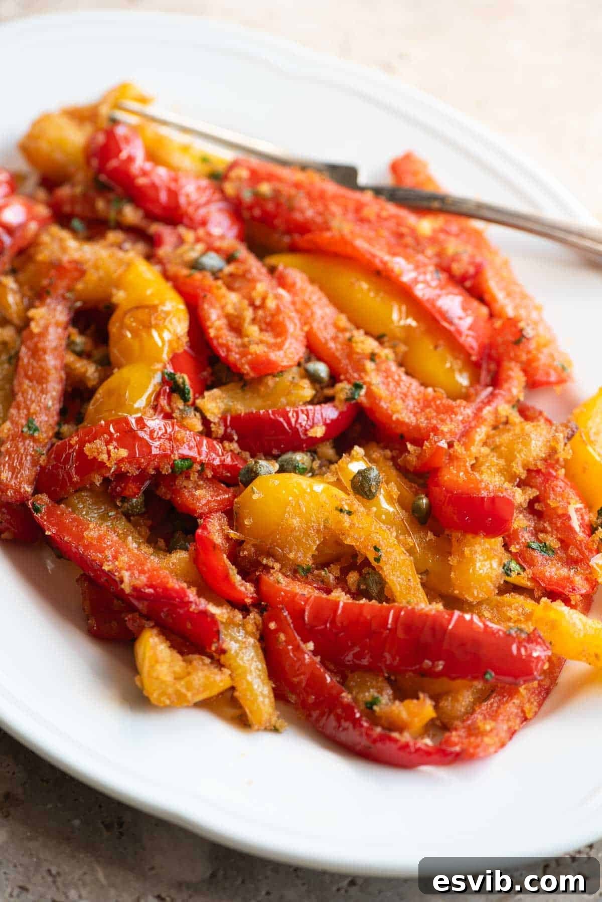 Rustic Bell Peppers with Garlic Crumbs 6 A close up side shot of mixed red and yellow peppers on a white servings dish with capers and breadcrumbs.