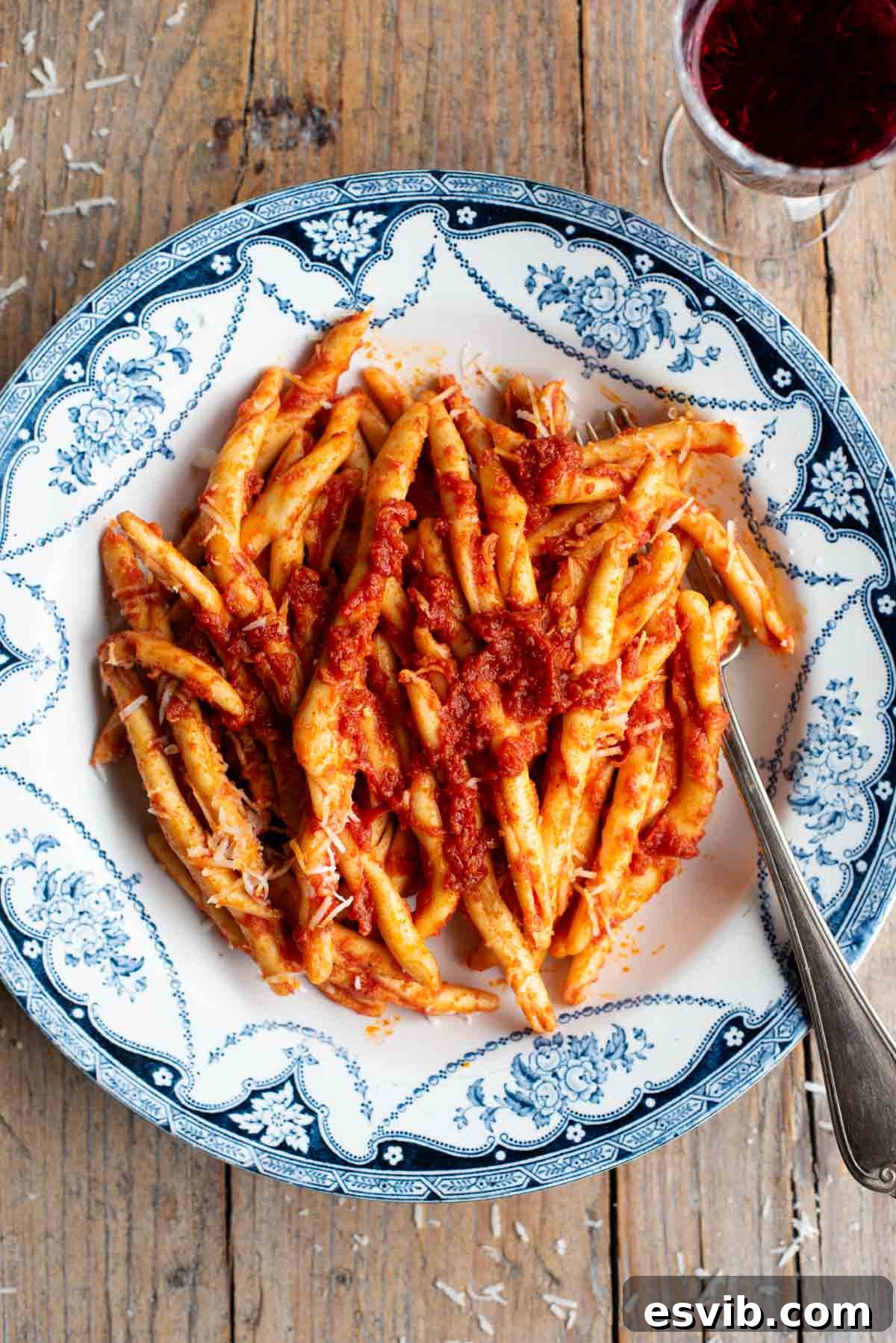 An overhead shot of spicy Nduja pasta (Fileja) in a blue and white bowl with a fork, the background is rustic wood.