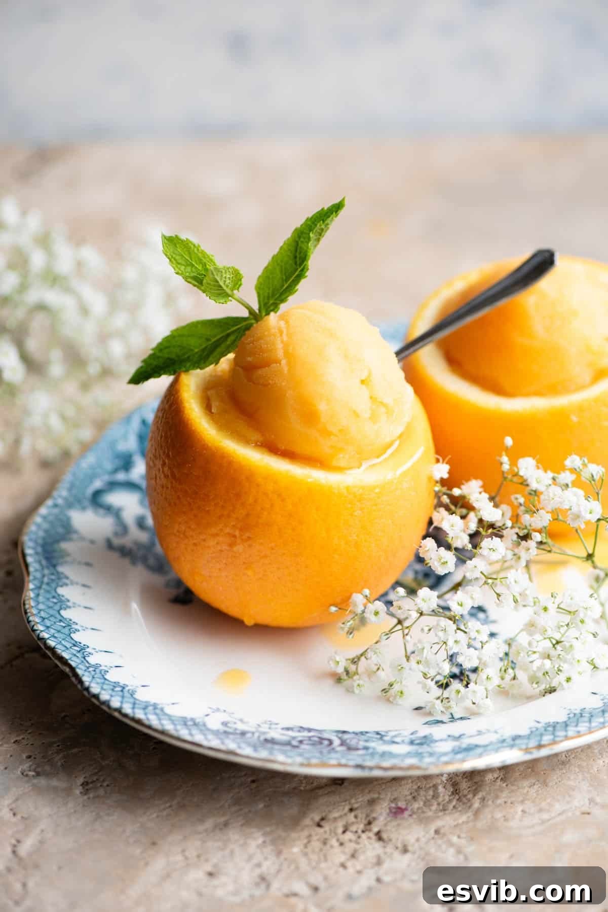 A scoop of vibrant orange sorbet served elegantly inside a hollowed-out orange peel, garnished with fresh mint leaves and a small spoon ready for tasting.