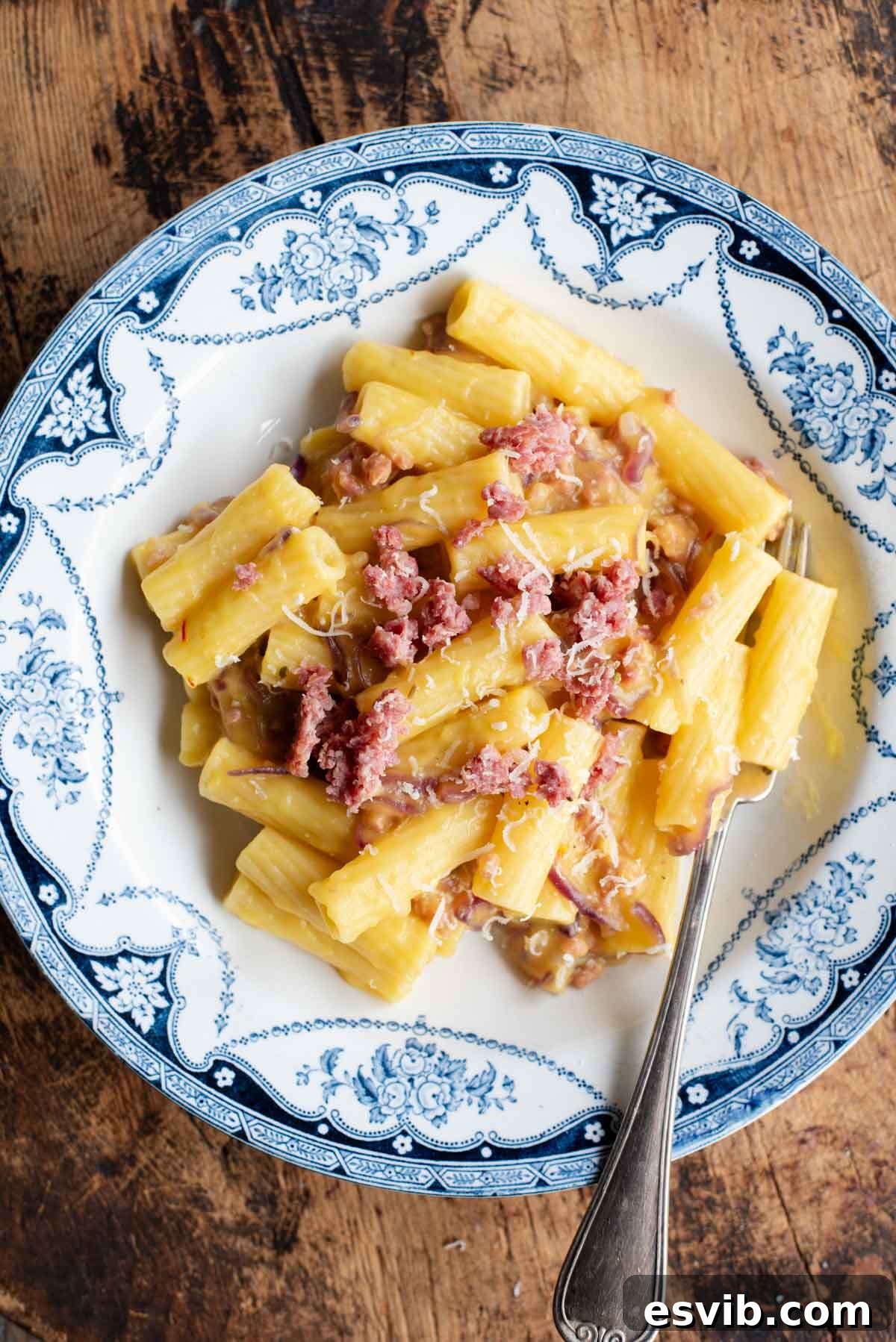 An overhead shot of a bowl of pasta with potato, saffron and sausage, the background is wooden.