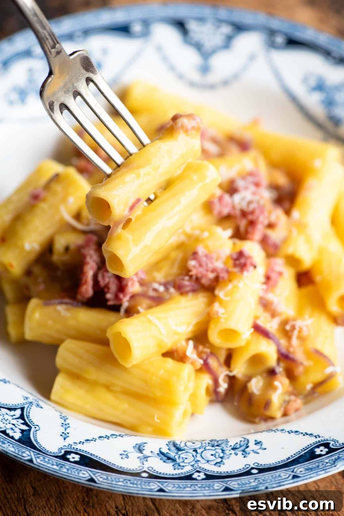 A close up of rigatoni on a fork hovering over a bowl of sausage and potato pasta.