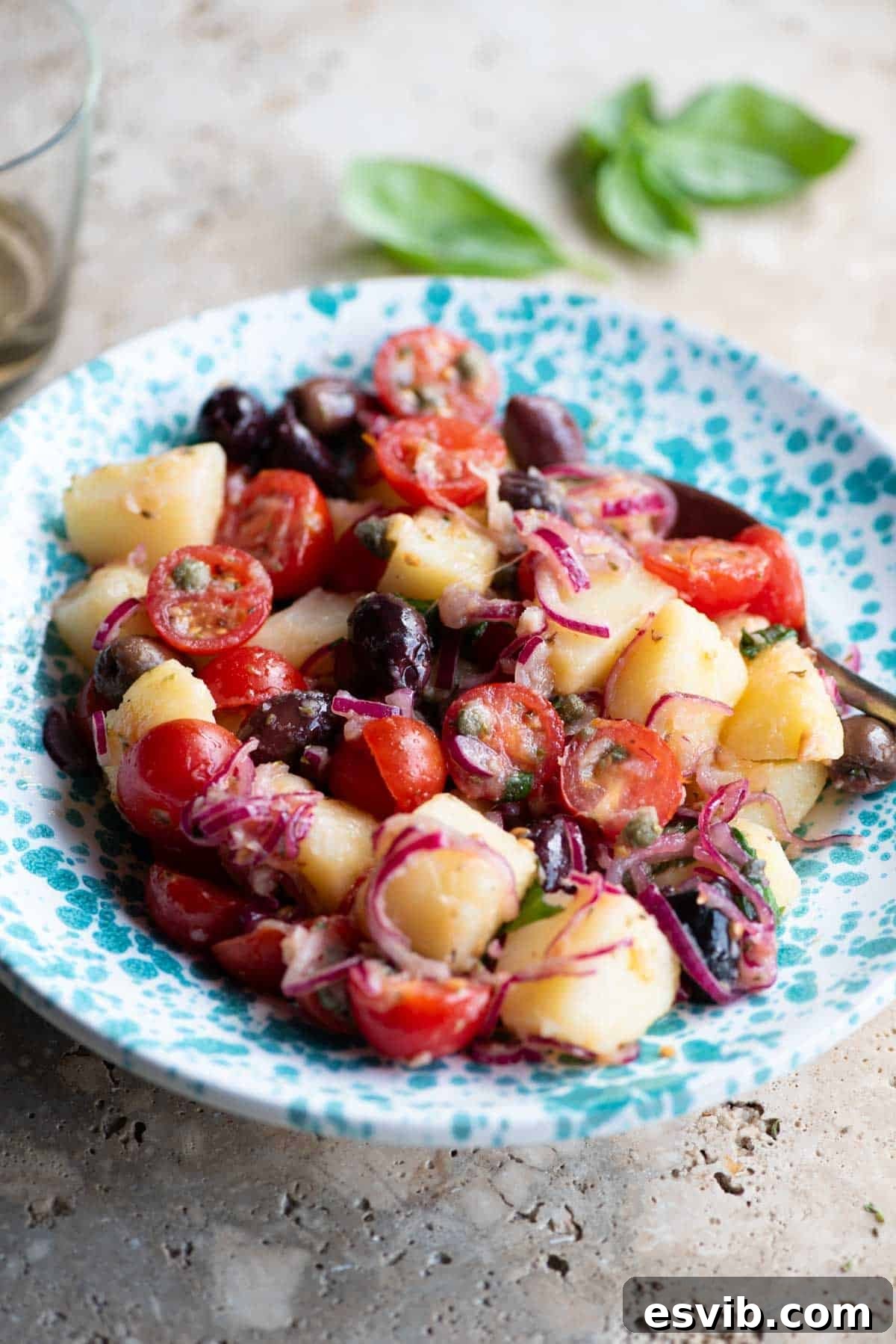 A vibrant Sicilian potato salad featuring potatoes, olives, tomatoes, and thinly sliced onions, presented beautifully in a blue and white patterned bowl.