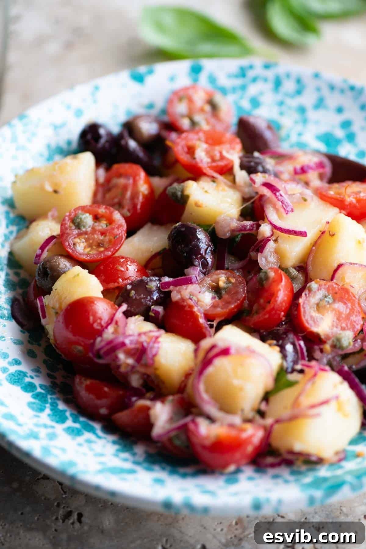 A detailed close-up shot of a traditional Sicilian potato salad (Insalata Pantesca) in a blue and white patterned bowl, highlighting the textures of potatoes, olives, and tomatoes.