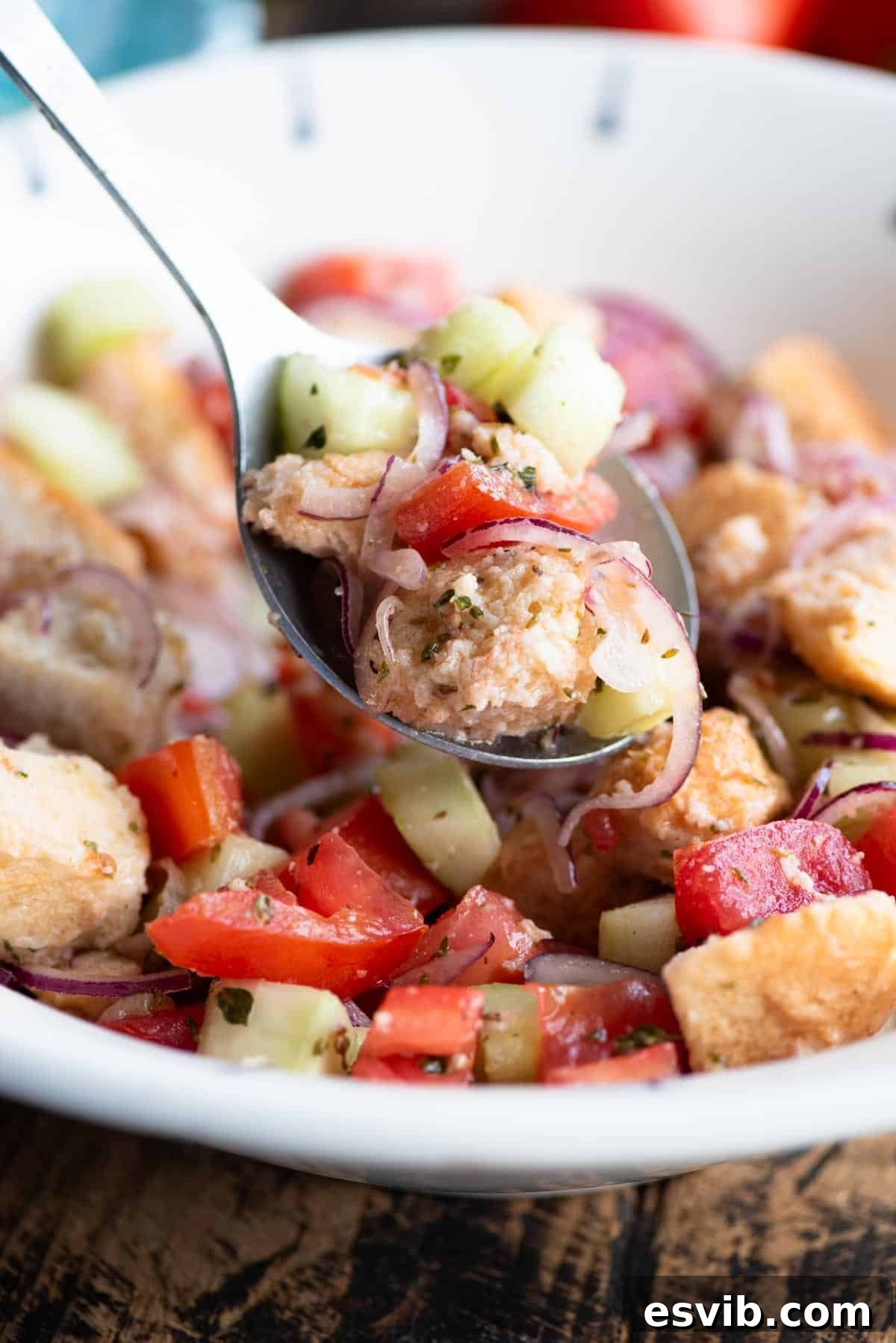 A close up of Cialledda salad with cucumber, tomatoes and bread on a serving spoon.