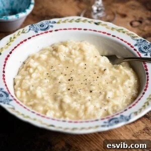 A close up cropped image of risotto alla Valdostana in a bowl ona. wooden surface.